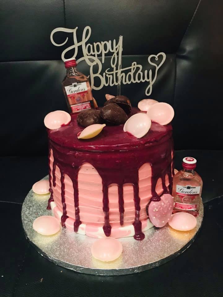 Round cake covered in pink buttercream with a chocolate drip on top with mini bottle of Gin, chocolates and happy birthday topper by creative cakes by kaz 