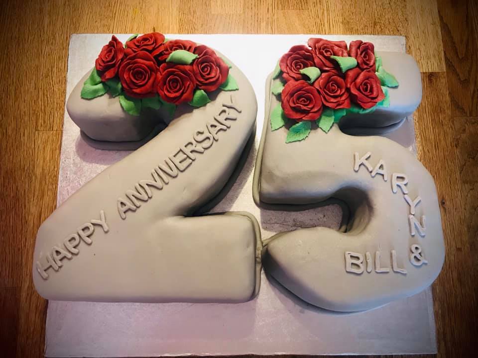 A number 25 cake covered in grey fondant with red fondant roses on each number 