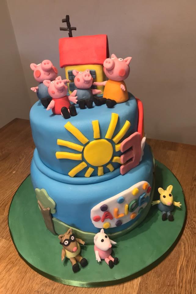 A two tier cake covered in fondant with fondant Peppa Pig characters and house on top by creative cakes by kaz 