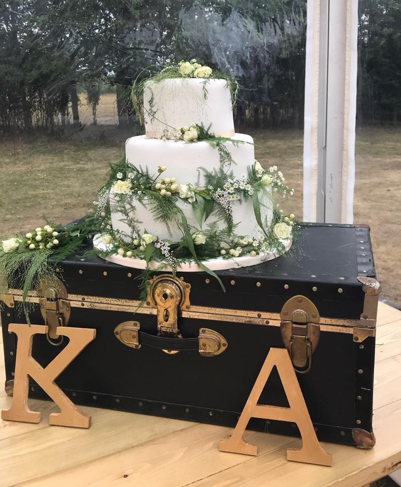 23 tier wedding cake covered in white fondant with real selection of flowers and greenery sitting on a black box with K and A initials by Creative Cakes by Kaz