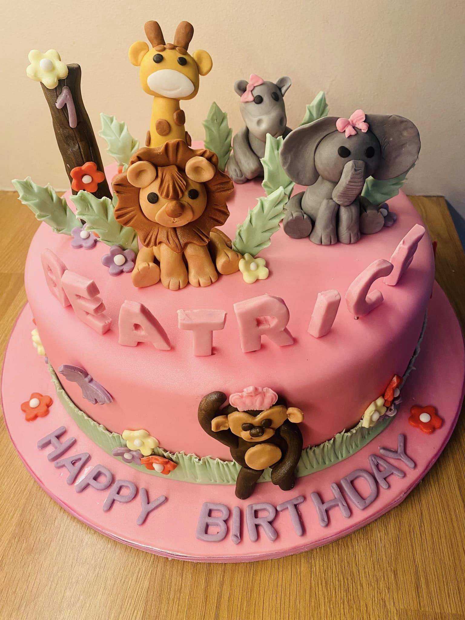 Round cake covered in pink fondant with lots of fondant animals on top, lion, elephant, giraffe rhino and monkey