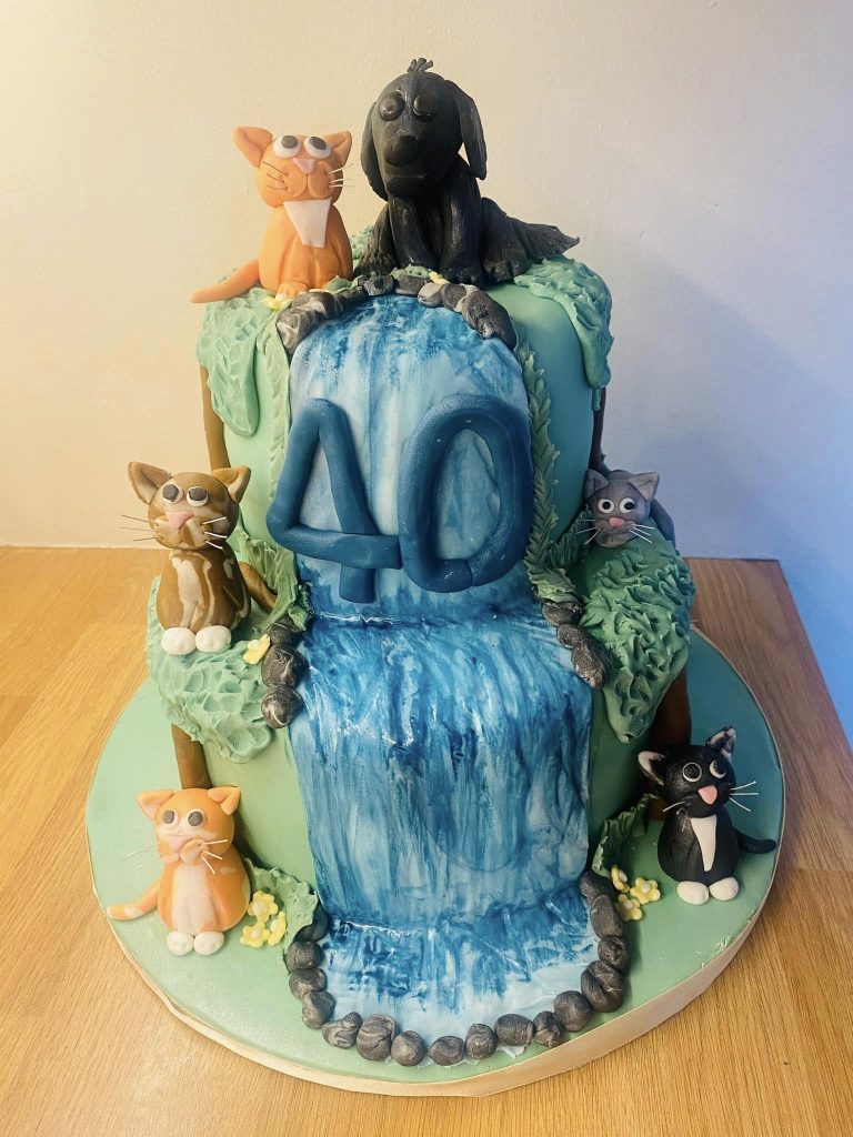 2 tier cake covered in fondant with a stream running down it and 9 fondant cakes 