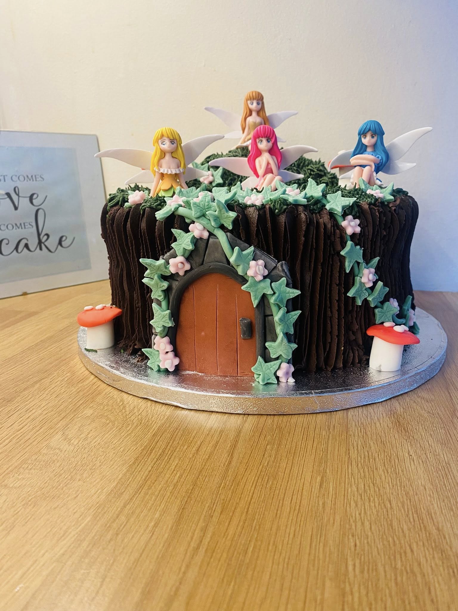 Round cake with a Fairy theme. 4 fairies sitting on top of cake with a secret  door Birthday & Novelty Cakes