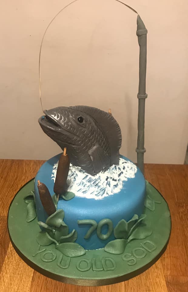 Round cake covered in blue fondant with  a  fondant fishes head and fishing line 