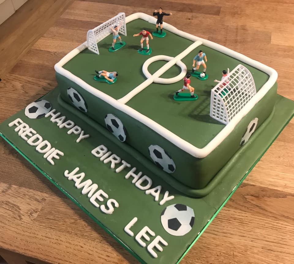 Rectangle cake covered in green fondant with a football pitch on top and plastic football players 