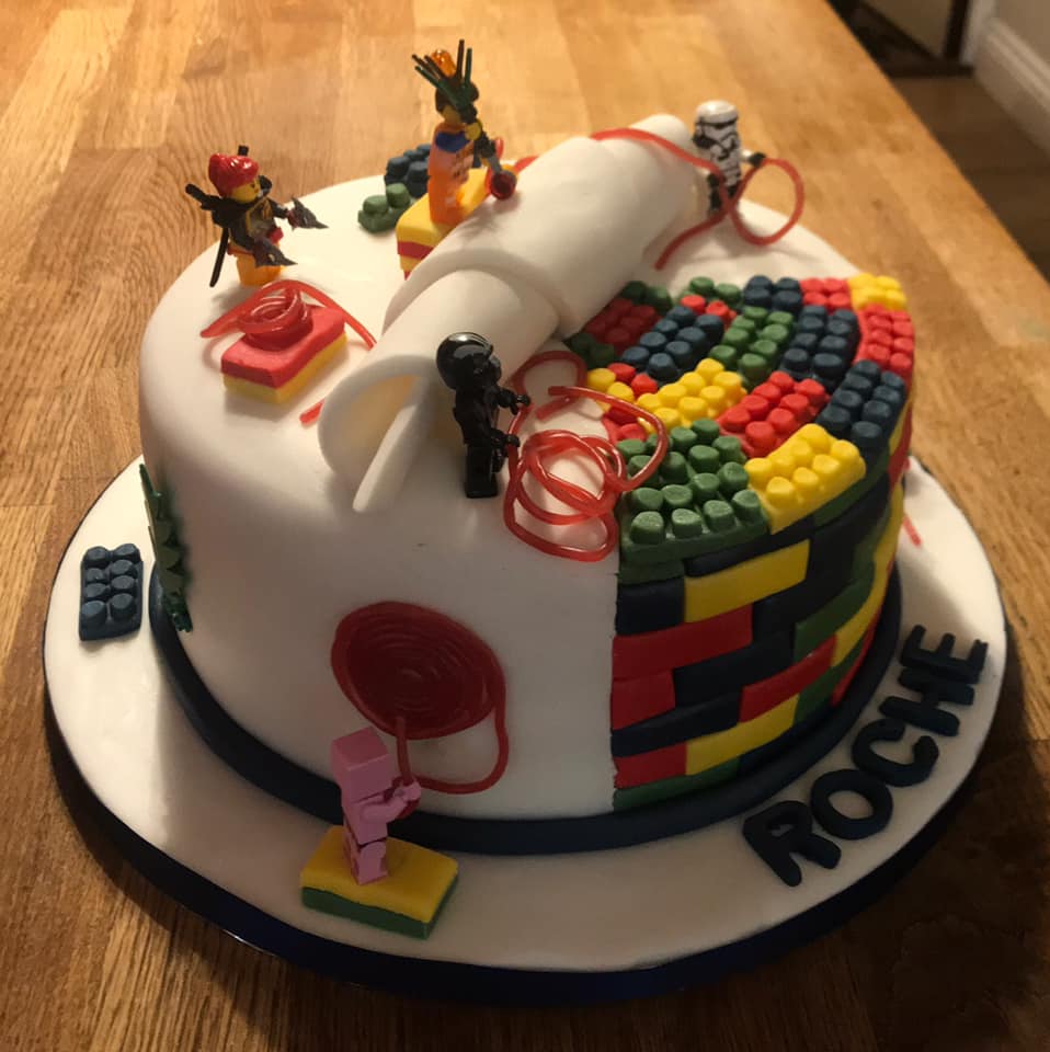 Cake covered in white fondant with some fondant lego blocks around it by creative cakes by kaz 