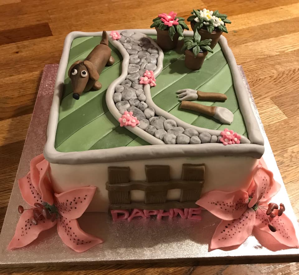 Square cake covered in fondant, fondant lilies in each corner with a fondant path,, flower pots and sausage top on top by creative cakes by kaz 
