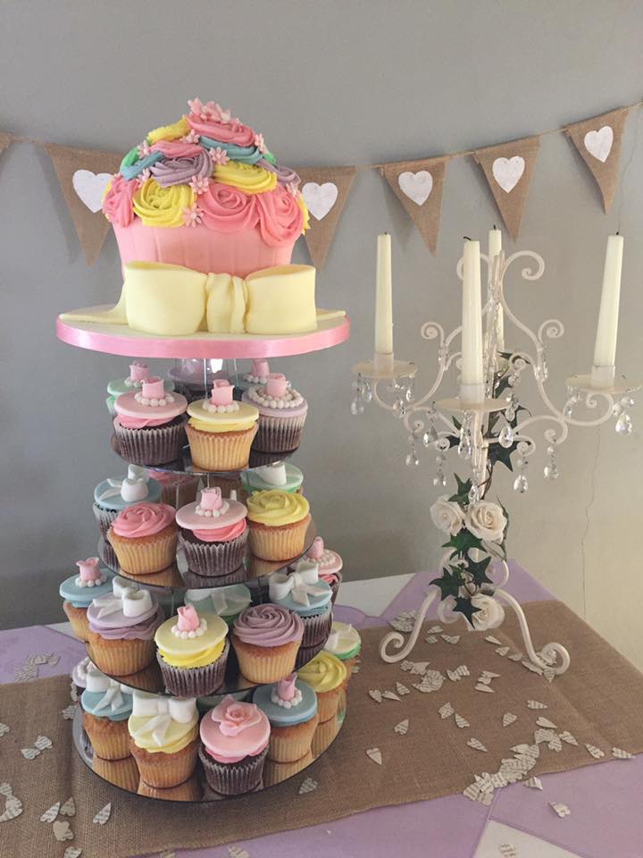 A giant cupcake covered in buttercream roses on pink, yellow and blue and underneath matching small cupcakes  sitting on a tower 