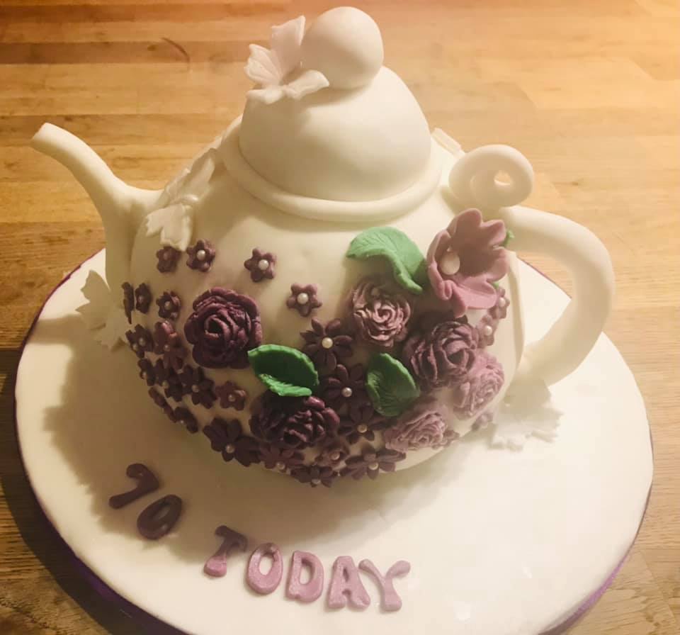 A cake shaped into a tea pot covered in fondant with fondant flowers and butterflies on it by creative cakes by kaz 