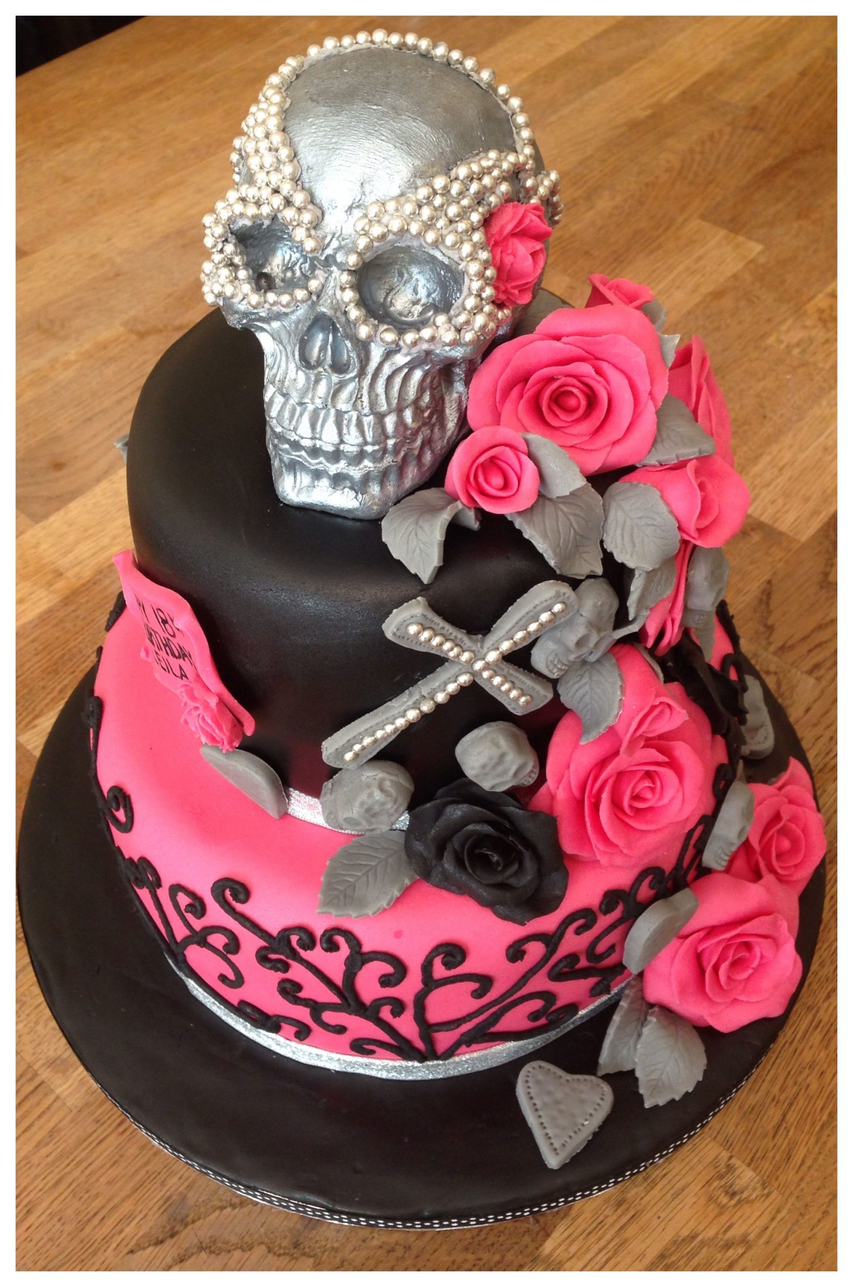 2 tier cake covered in black fondant with pink fondant roses, grey skulls around the side and a large chocolate skull on top 
