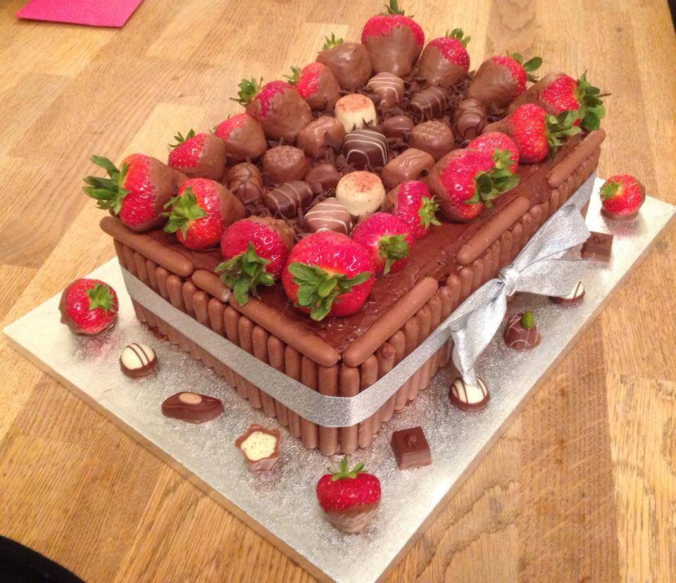rectangle cake covered in chocolate buttercream with chocolate fingers around the sides and strawberries and chocolate on top 