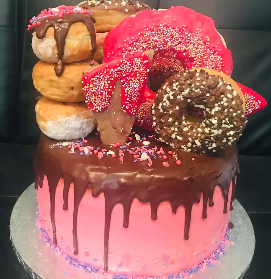 Cake covered in pink buttercream with a chocolate dip, then a selection of doughnuts on top by creative cakes by kaz 