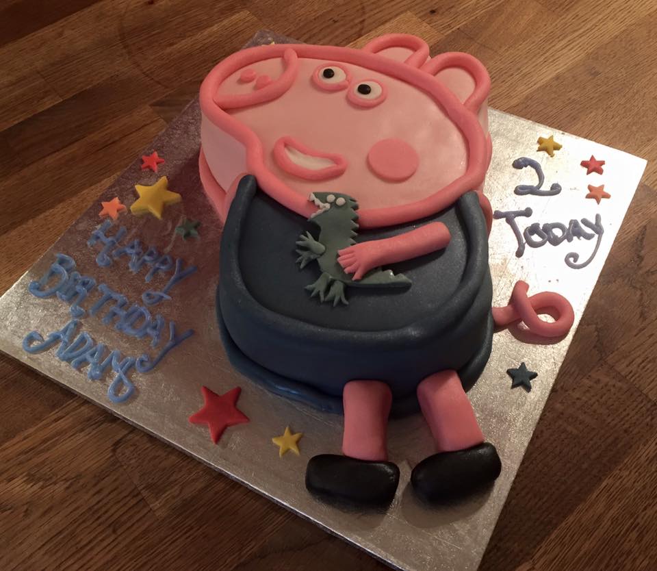 A cake in the shape of Peppa Pig covered in blue and pink fondant holding a dinosaur