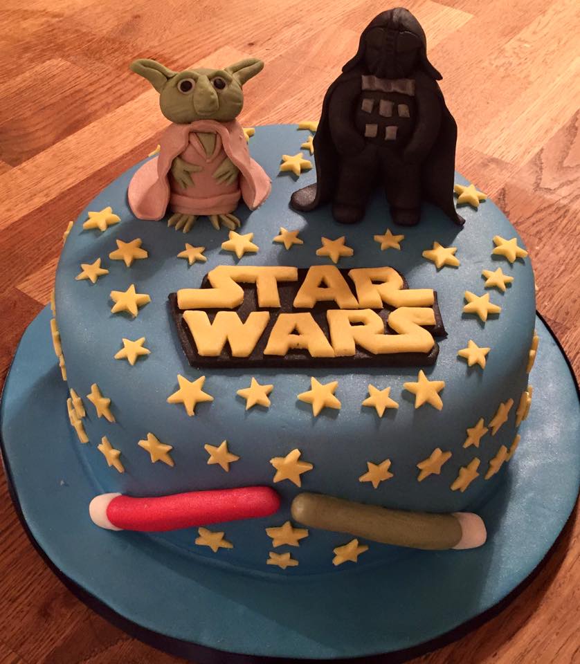 Round cake covered in fondant with a fondant star wars characters on top and light sabers around the sides 