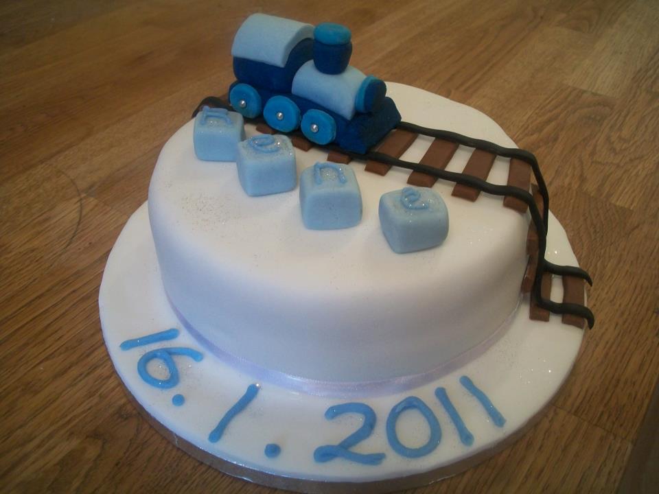 round christening cake with a fondant blue train on top of a train track and number blocks 
