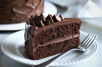 Slice of a rich chocolate cake with a chocolate buttercream filling sitting on a white plate next to a forl 